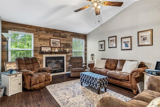 living area with dark wood-type flooring, vaulted ceiling, ceiling fan, wooden walls, and a large fireplace