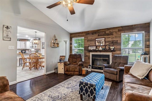 living room with lofted ceiling, a tile fireplace, a healthy amount of sunlight, and ceiling fan with notable chandelier