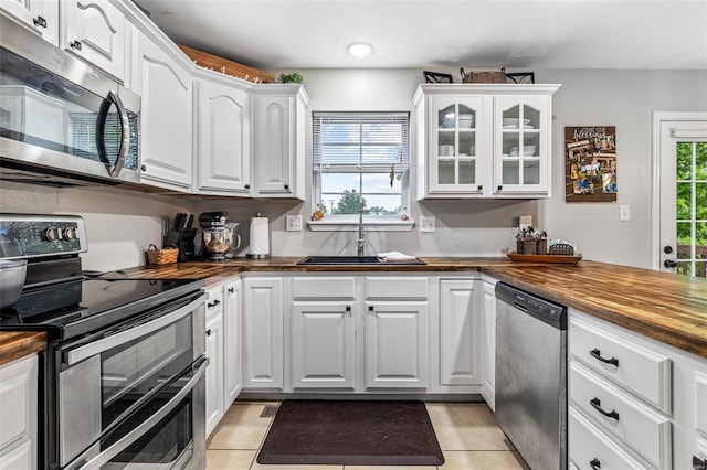 kitchen featuring butcher block countertops, stainless steel appliances, a sink, and glass insert cabinets