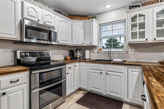 kitchen featuring glass insert cabinets, butcher block counters, a sink, white cabinetry, and stainless steel appliances