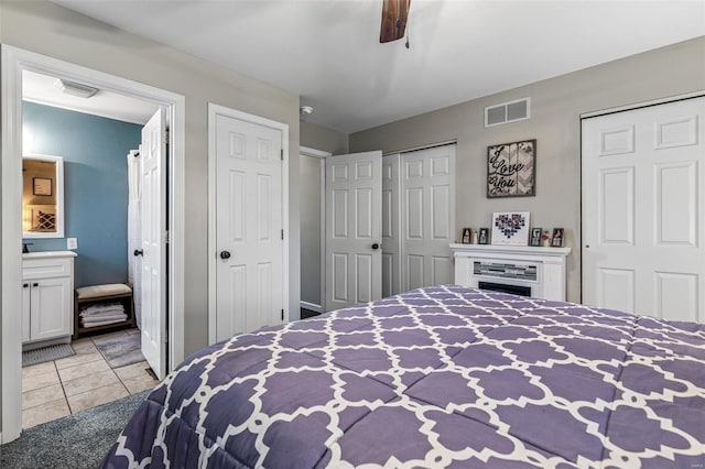 tiled bedroom with a ceiling fan, ensuite bathroom, multiple closets, and visible vents