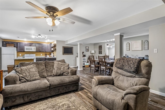 living area with ornate columns, track lighting, dark wood-style floors, a ceiling fan, and baseboards