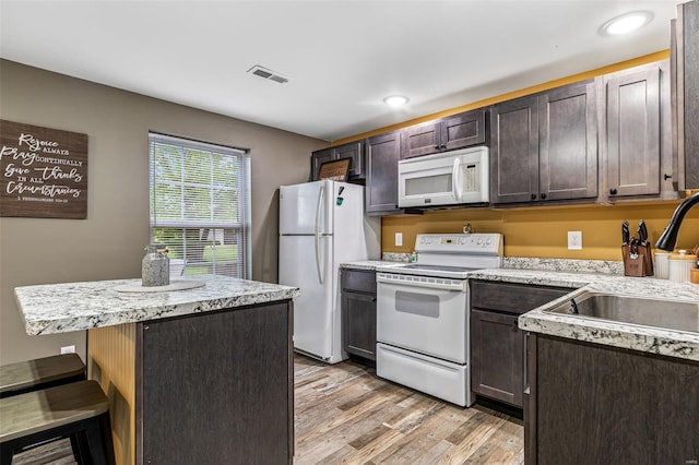 kitchen featuring dark brown cabinets, white appliances, visible vents, a sink, and light wood-style floors