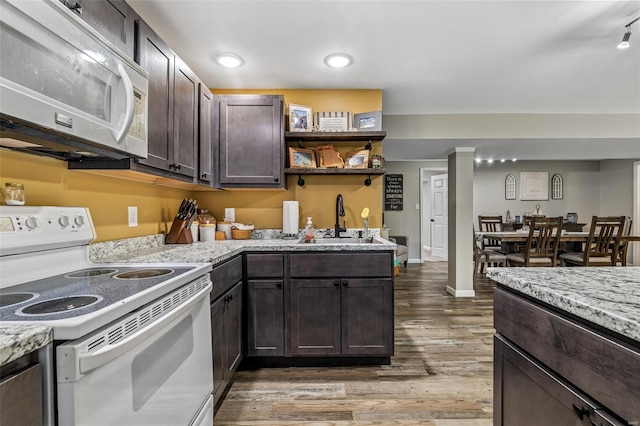kitchen with dark brown cabinets, white appliances, light stone counters, a sink, and wood finished floors