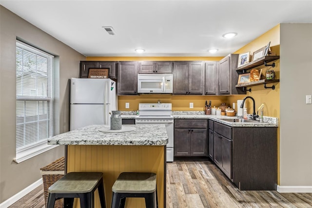 kitchen featuring a sink, dark brown cabinetry, white appliances, and baseboards