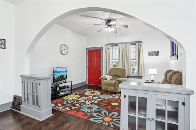 living area featuring arched walkways, baseboards, a ceiling fan, and dark wood-type flooring