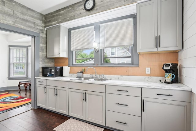 kitchen with black microwave, wood walls, dark wood finished floors, a sink, and gray cabinetry