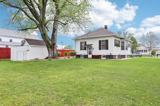 rear view of house with fence, an outbuilding, a chimney, and a yard