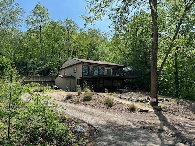 back of house with a deck, a shed, an outbuilding, a chimney, and a wooded view