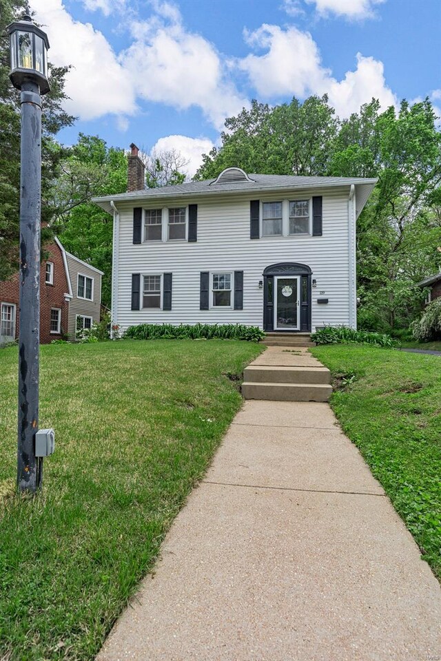 colonial-style house featuring a front yard and a chimney