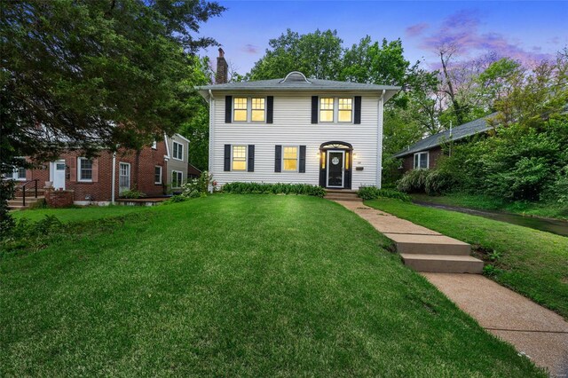 colonial inspired home featuring a lawn and a chimney