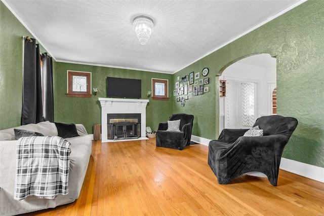 living area with a fireplace with flush hearth, arched walkways, ornamental molding, a textured wall, and hardwood / wood-style floors