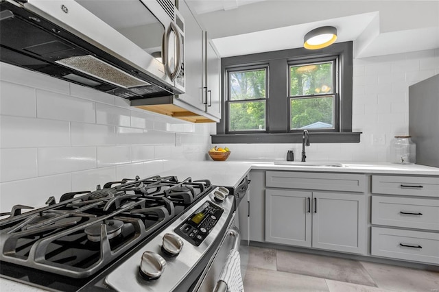 kitchen with a sink, light countertops, gas range, backsplash, and gray cabinetry