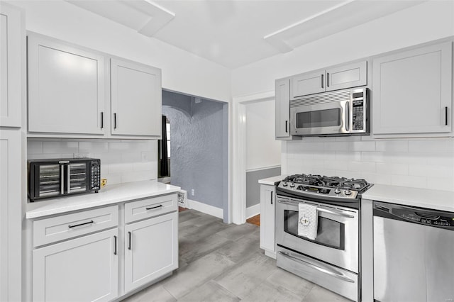 kitchen featuring a toaster, baseboards, light countertops, tasteful backsplash, and appliances with stainless steel finishes
