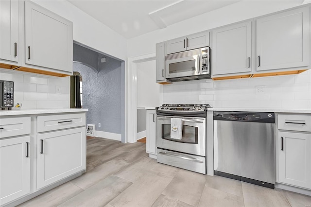 kitchen with appliances with stainless steel finishes, light countertops, baseboards, decorative backsplash, and visible vents