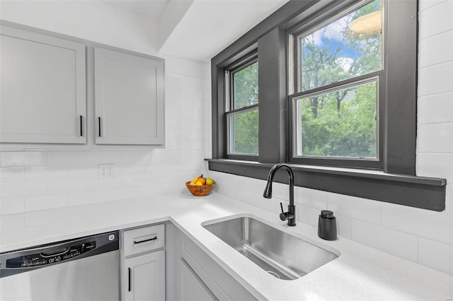 kitchen with light stone countertops, decorative backsplash, a sink, and dishwasher