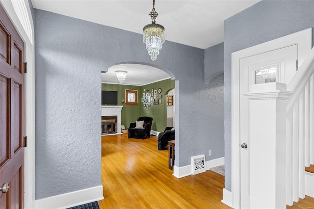 foyer entrance with a textured wall, a fireplace, arched walkways, baseboards, and light wood-type flooring
