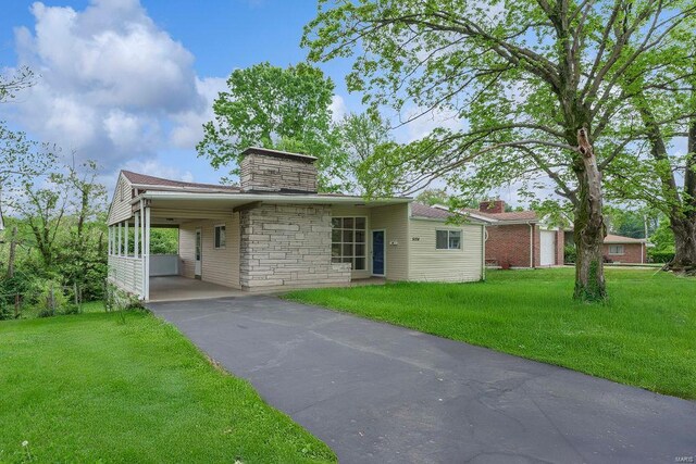 view of front of house featuring a carport, a chimney, driveway, and a front lawn