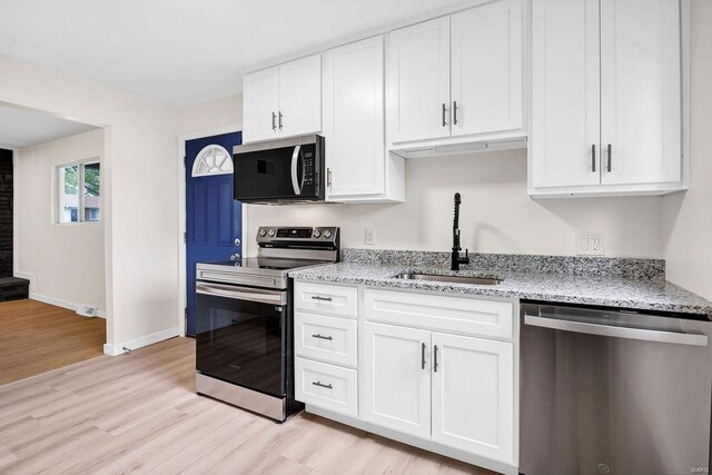 kitchen with a sink, white cabinets, stainless steel appliances, and light wood finished floors