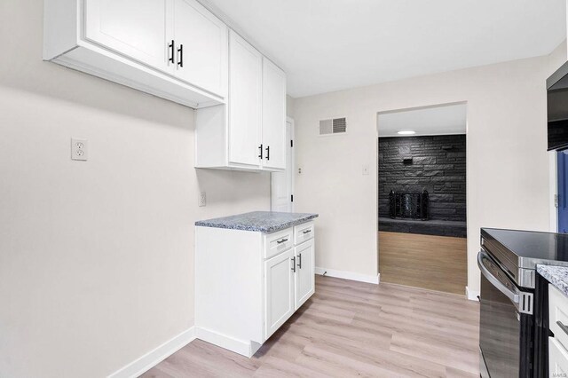 kitchen featuring light wood-style floors, stainless steel range with electric stovetop, white cabinetry, baseboards, and visible vents