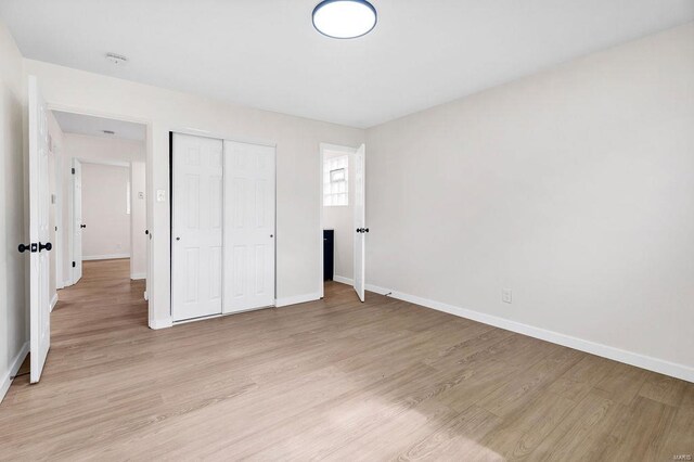 unfurnished bedroom with a closet, baseboards, and light wood-type flooring