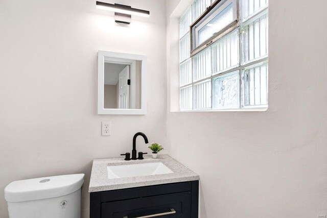 half bathroom with toilet, a healthy amount of sunlight, and vanity