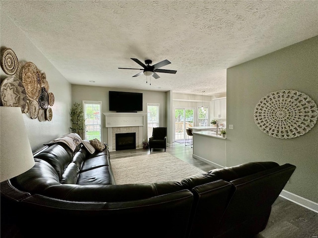 living room with ceiling fan, a textured ceiling, baseboards, and a tiled fireplace