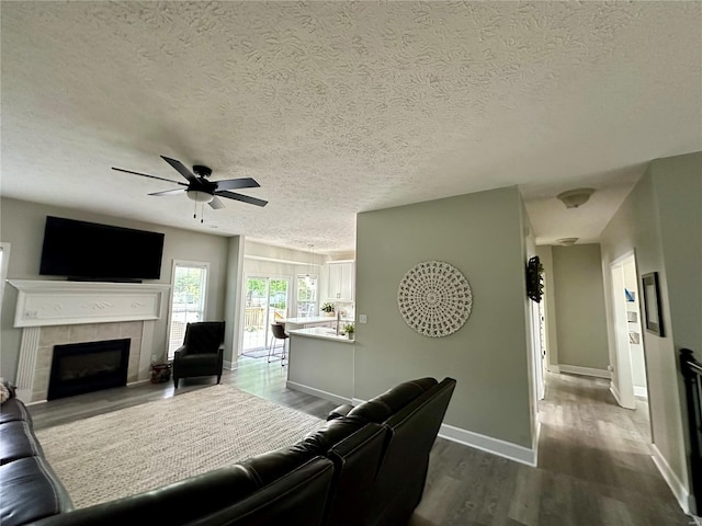 living area with a textured ceiling, a tile fireplace, a ceiling fan, and dark wood finished floors