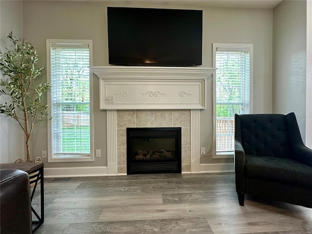 sitting room with a tiled fireplace, wood finished floors, baseboards, and visible vents