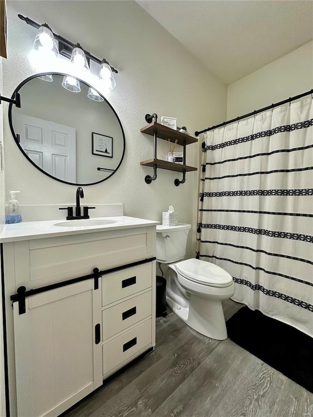 full bath with toilet, wood finished floors, a shower with shower curtain, a textured wall, and vanity