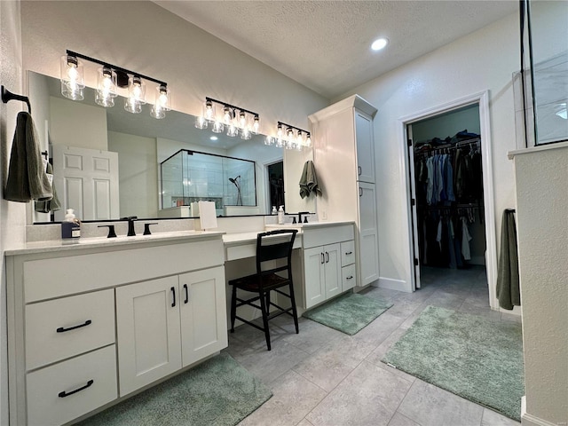 bathroom with a sink, a textured ceiling, a stall shower, a walk in closet, and two vanities