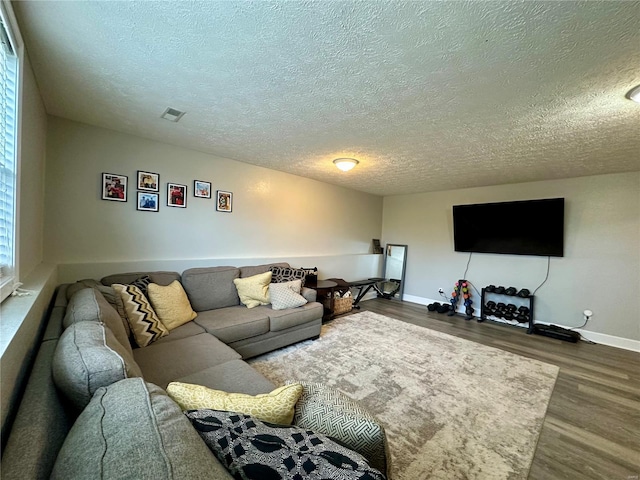 living room with a textured ceiling, visible vents, wood finished floors, and baseboards
