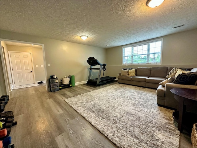 living room featuring baseboards, visible vents, a textured ceiling, and wood finished floors