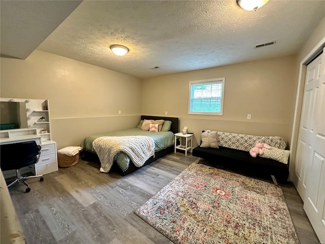 bedroom featuring a closet, visible vents, a textured ceiling, and wood finished floors
