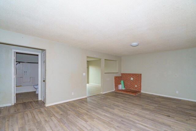 unfurnished living room with a textured ceiling, wood finished floors, and baseboards