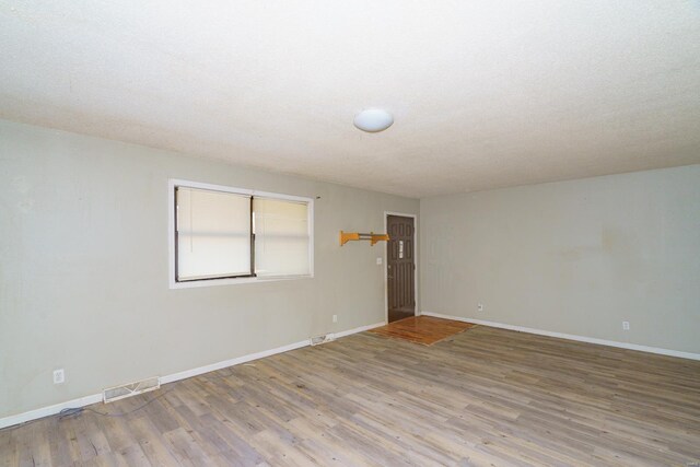 unfurnished room featuring a textured ceiling, baseboards, visible vents, and wood finished floors