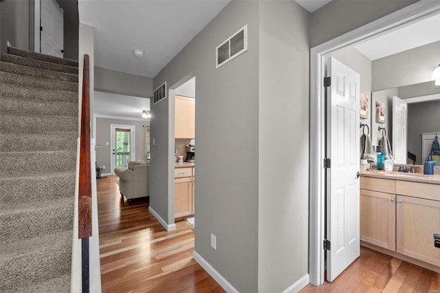 corridor with stairway, light wood finished floors, and visible vents