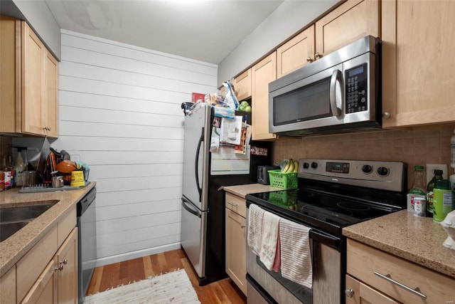 kitchen with light brown cabinetry, stainless steel appliances, light stone countertops, and light wood-style flooring