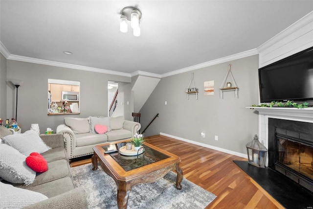 living area with baseboards, a glass covered fireplace, ornamental molding, and wood finished floors