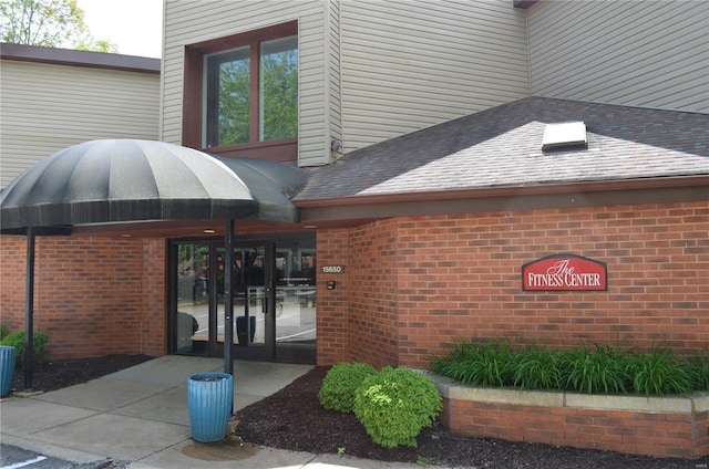 view of exterior entry with a shingled roof and brick siding