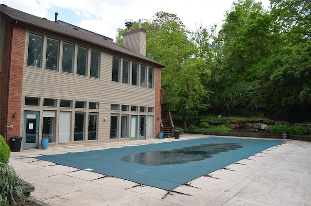 rear view of house featuring stairs, a covered pool, brick siding, a chimney, and a patio area