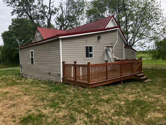 rear view of property featuring a wooden deck, a yard, and metal roof