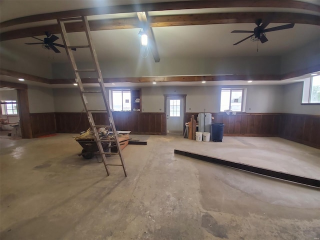 basement with a wainscoted wall, ceiling fan, and wood walls