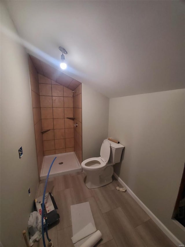 full bath featuring vaulted ceiling, wood finished floors, a tile shower, and toilet
