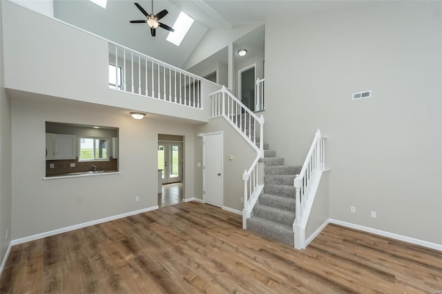 unfurnished living room featuring a ceiling fan, a skylight, wood finished floors, and stairway