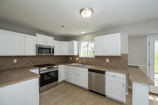 kitchen with decorative backsplash, appliances with stainless steel finishes, a sink, white cabinets, and a peninsula