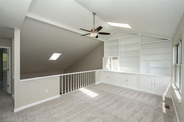 bonus room with vaulted ceiling with skylight, a ceiling fan, visible vents, built in features, and carpet floors