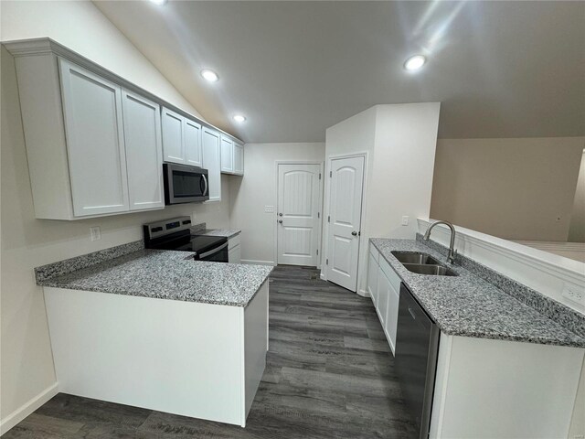 kitchen with a peninsula, light stone countertops, a sink, dark wood finished floors, and stainless steel appliances