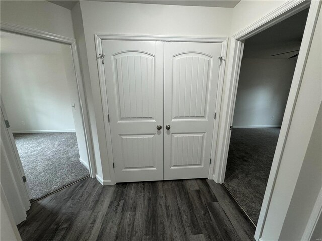 hallway featuring baseboards, dark colored carpet, and dark wood-style floors