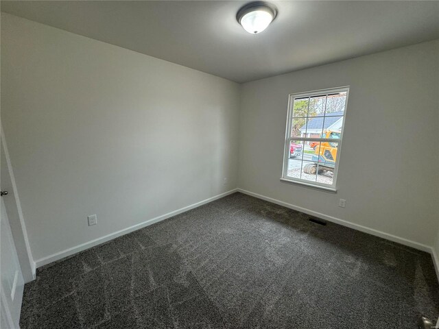 empty room with baseboards, dark carpet, and visible vents